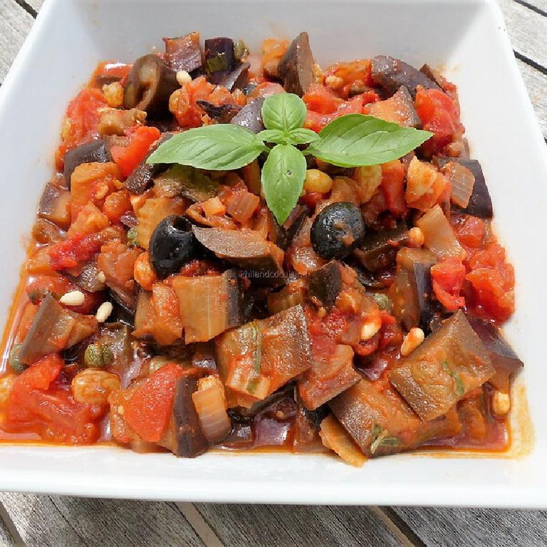 sur une plat rectangulaire en faïence blanche, une caponata sicilienne et en décoration quelques olives noires et 4 feuilles de basilic