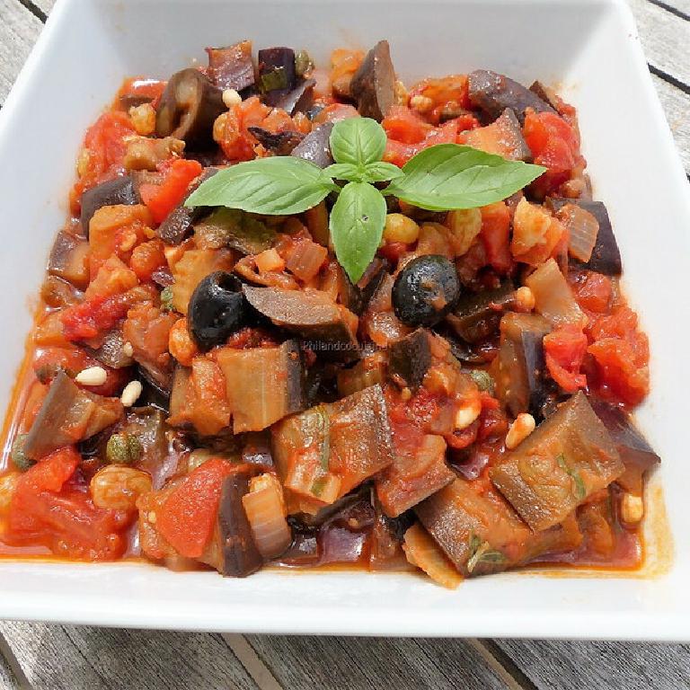 sur une plat rectangulaire en faïence blanche, une caponata sicilienne et en décoration quelques olives noires et 4 feuilles de basilic