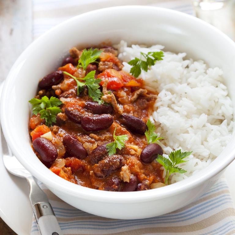 Une assiette creuse remplie de chili con carne pour moitié et de riz pilav pour le restant