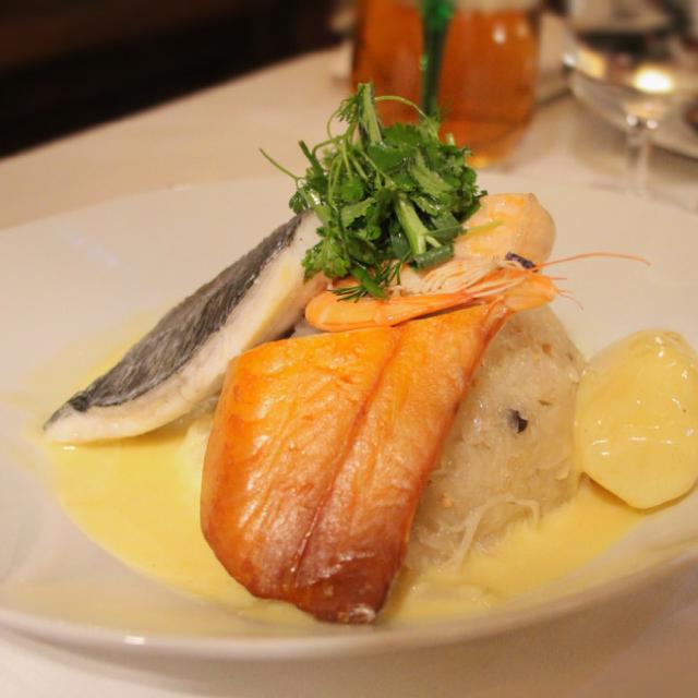 une assiette avec de la choucroute et de la sauce au fond ; par dessus, trois morceaux de poissons, une pomme de terre