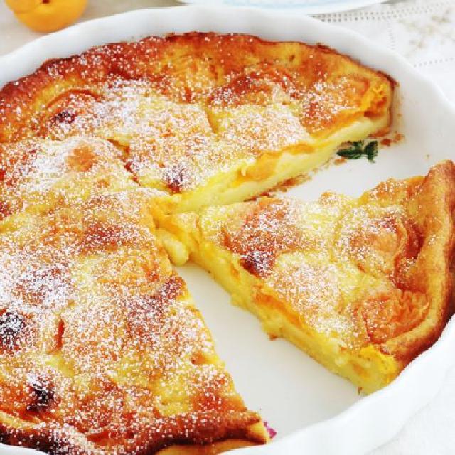 image d'un clafoutis aux abricots, encore dans son plat de cuisson, avec une portion déjà coupée.