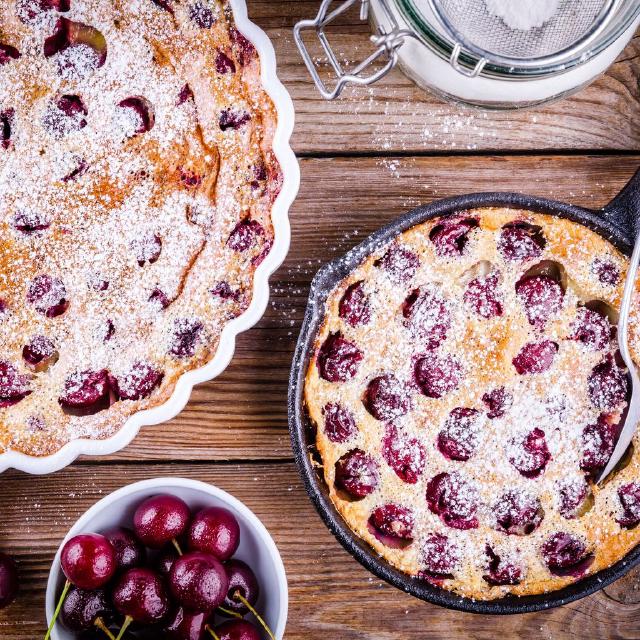 photo de deux clafoutis aux cerises posés sur une table en bois, avec un bol contenant quelques cerises.