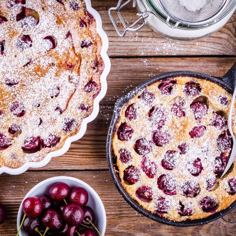 photo de deux clafoutis aux cerises posés sur une table en bois, avec un bol contenant quelques cerises.
