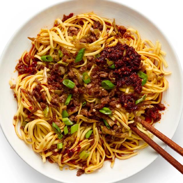 une assiette de nouilles chinoises, couverte de viande hachée et de sauce pimentée, avec deux baguettes sur le bord
