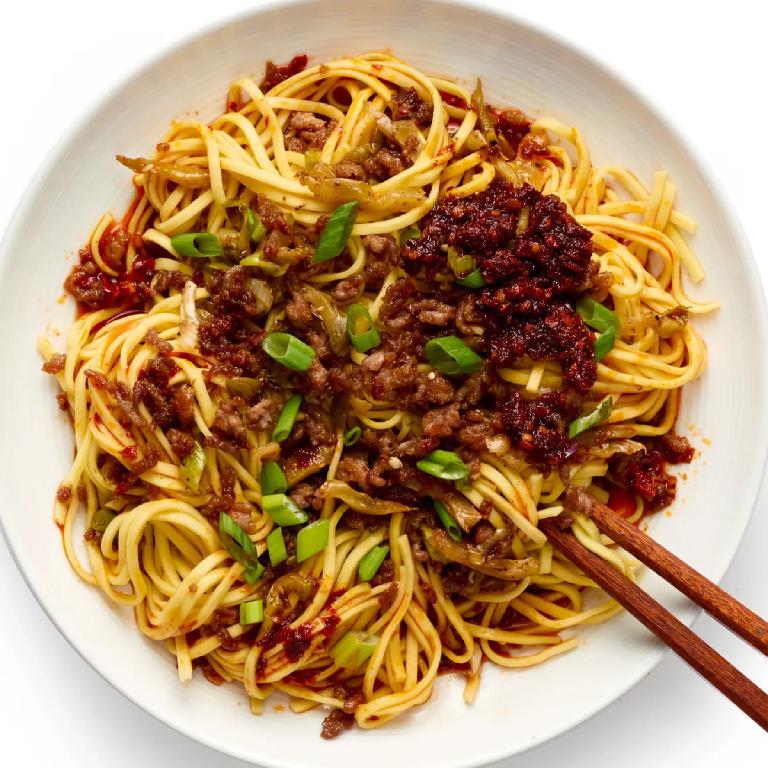 une assiette de nouilles chinoises, couverte de viande hachée et de sauce pimentée, avec deux baguettes sur le bord