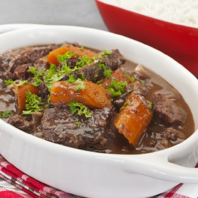 dans un grand plat en faïence blanche, des morceaux de viande dans la sauce de la daube provençale ; quelques carottes en tronçons et des pluches de cerfeuil pour agrémenter le plat