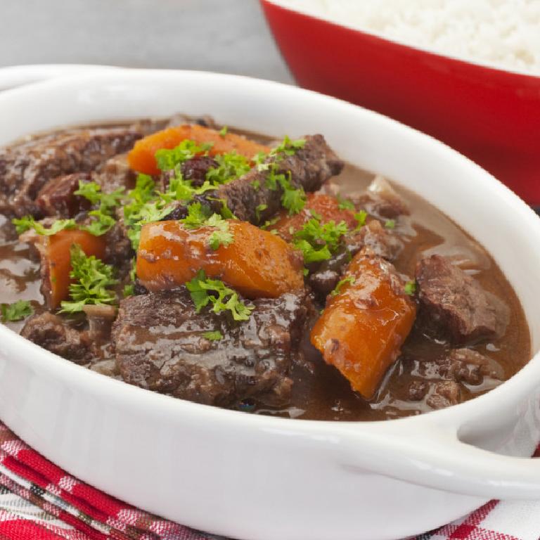 dans un grand plat en faïence blanche, des morceaux de viande dans la sauce de la daube provençale ; quelques carottes en tronçons et des pluches de cerfeuil pour agrémenter le plat