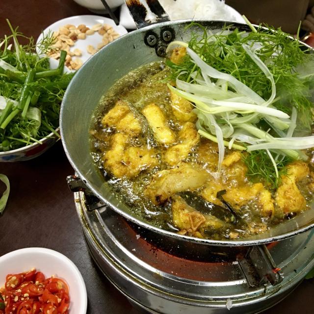 un wok sur de la braise avec du poisson cha ca, frit avec des vermicelles de riz