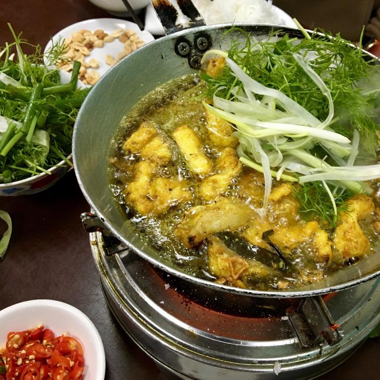 un wok sur de la braise avec du poisson cha ca, frit avec des vermicelles de riz
