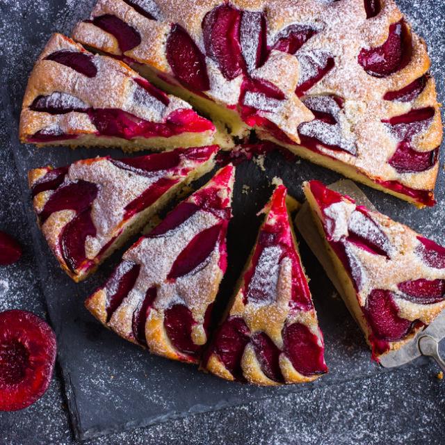 une gâteau aux prunes parsemé de sucre glace, avec des parts déjà coupées