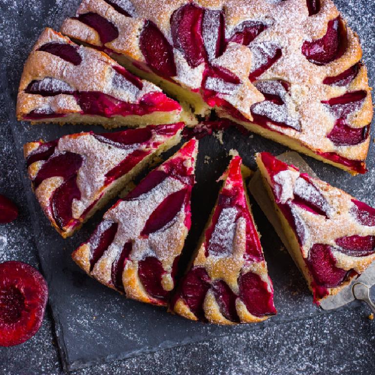 une gâteau aux prunes parsemé de sucre glace, avec des parts déjà coupées