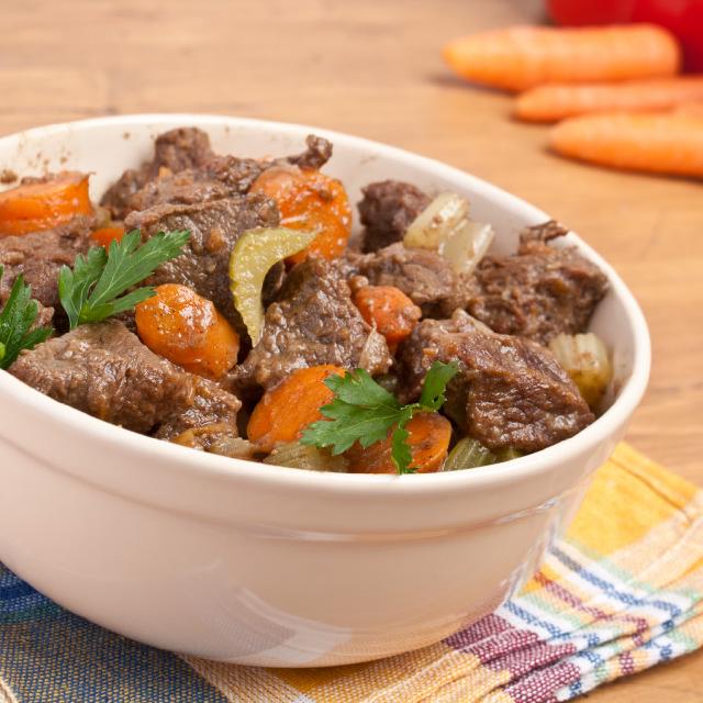 dans un plat ovale en céramique blanche, des morceaux de joue de boeuf, avec quelques morceaux de carotte et de céleri branche ; deux feuilles de persil pour décorer le tout