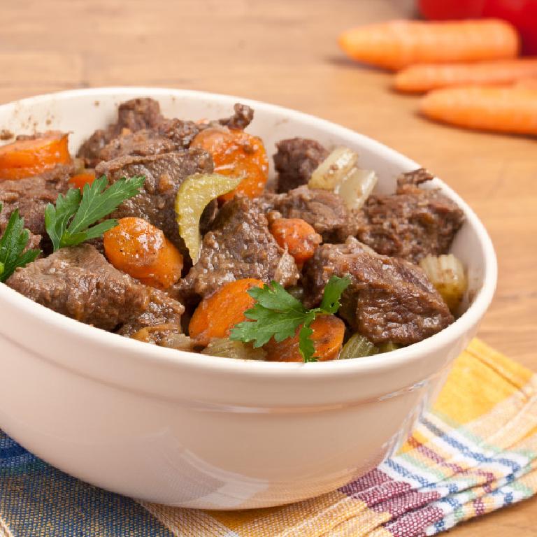 dans un plat ovale en céramique blanche, des morceaux de joue de boeuf, avec quelques morceaux de carotte et de céleri branche ; deux feuilles de persil pour décorer le tout