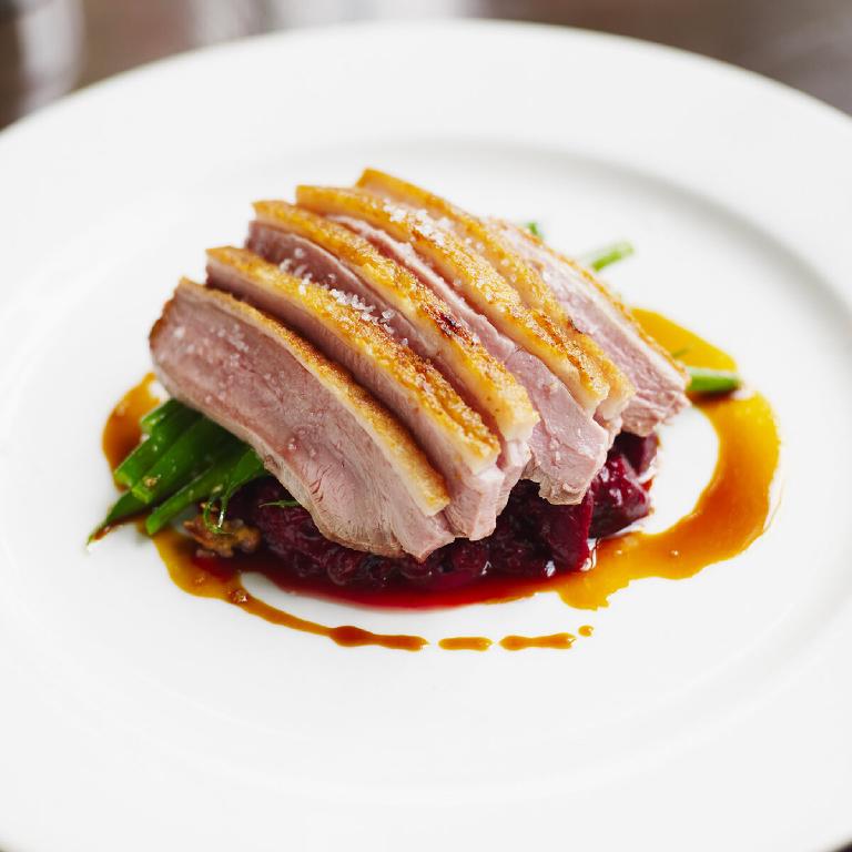 quelques tranches de magret de canard laqué rôti au four, dans une assiette blanche