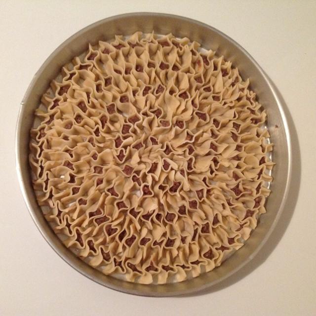Des mantis en forme de petite barquettes tassés les uns contre les autres dans un plat rond en métal, donnant une impression très graphique à l'ensemble