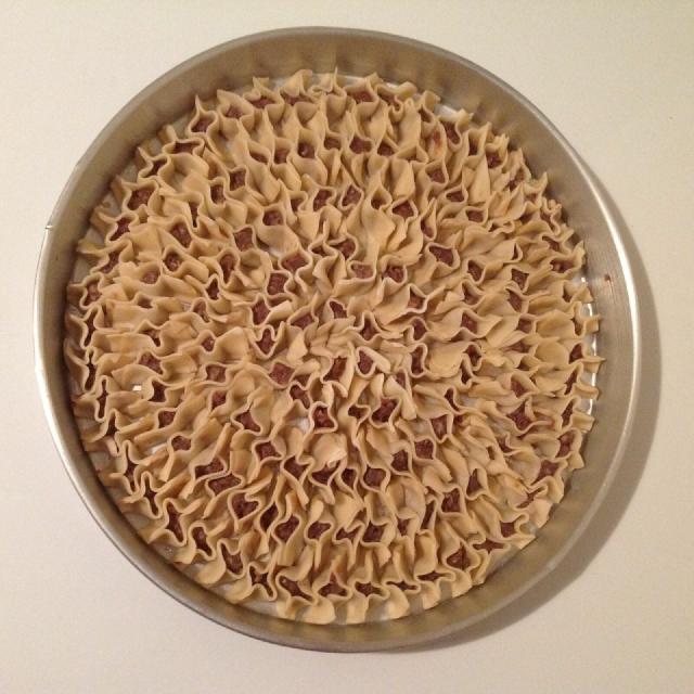 Des mantis en forme de petite barquettes tassés les uns contre les autres dans un plat rond en métal, donnant une impression très graphique à l'ensemble