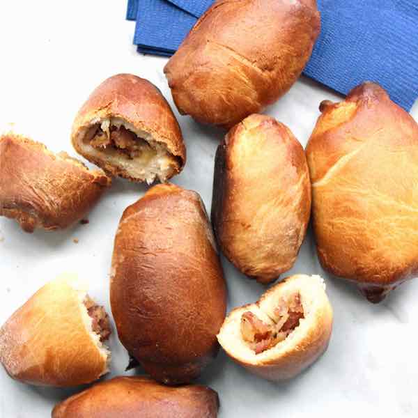 sur une assiette, des piragi, petits pâtés farcis d'origine lettone ; certains sont entiers, d'autres coupé en deux pour montrer la farce