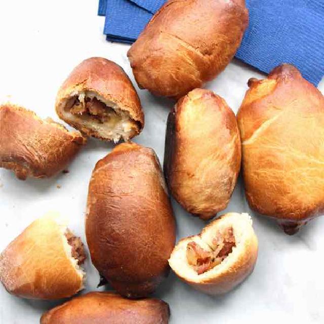 sur une assiette, des piragi, petits pâtés farcis d'origine lettone ; certains sont entiers, d'autres coupé en deux pour montrer la farce