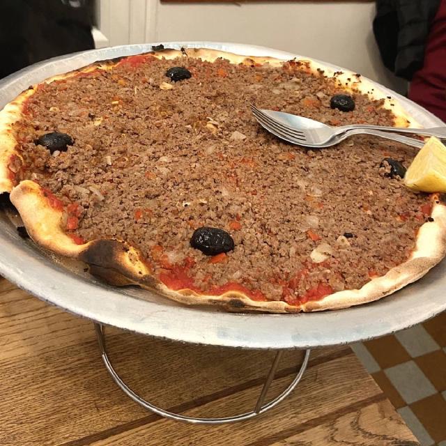 Sur un plateau, une pizza couverte de viande hachée, avec quelques olives et un quartier de citron