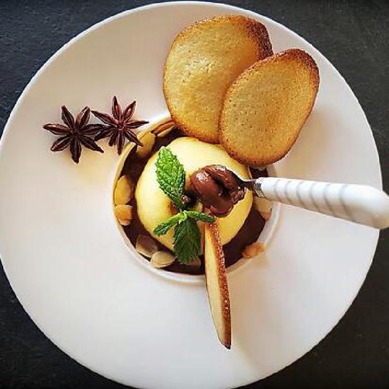Une coupelle avec une pomme pochée au vin blanc et un sauce d'accompagnement