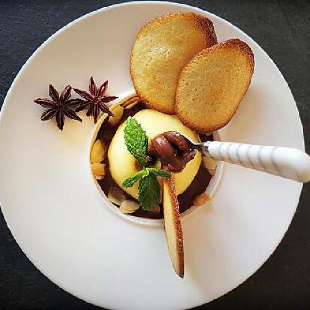 Une coupelle avec une pomme pochée au vin blanc et un sauce d'accompagnement