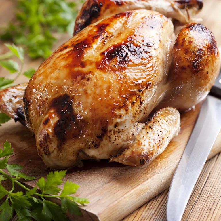 sur une planche à découper, un beau poulet fermier rôti, doré à point ; sur le devant de la photo, un couteau à découper
