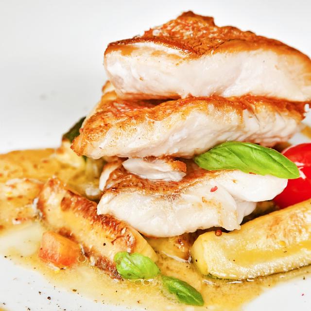 morceaux de queues de lotte dans une assiette, nappés de sauce, avec quelques feuille de basilic en décoration