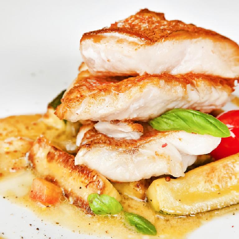 morceaux de queues de lotte dans une assiette, nappés de sauce, avec quelques feuille de basilic en décoration