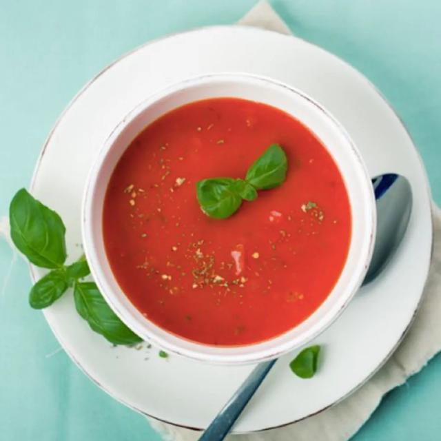 une assiette de soupe de tomate avec une feuille de basilic