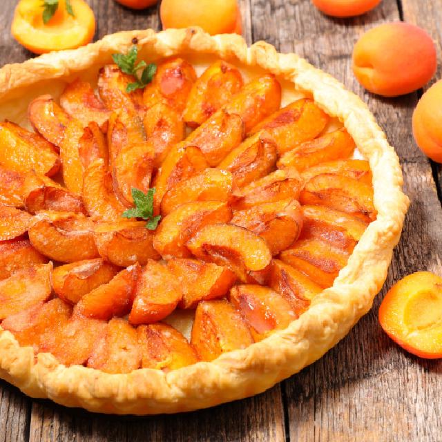 image d'une tarte à l'abricot posée sur une table en bois, avec quelques abricots de part et d'autre