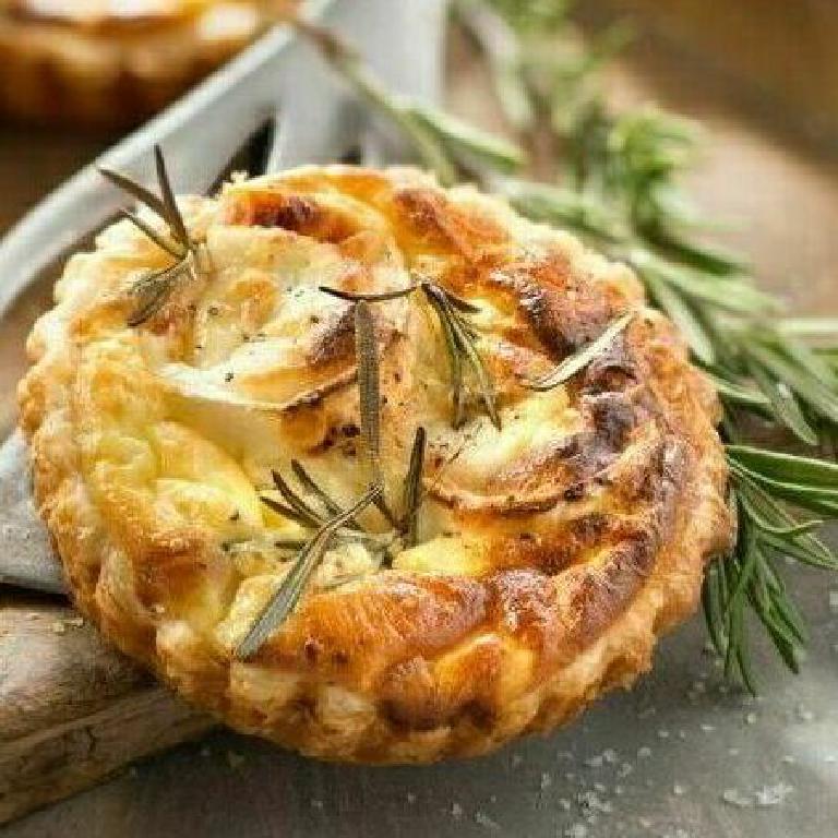 sur une planche à découper une tartelette au parmesan et au fromage de chèvre légèrement gratinée, avec des brins de romarin en décoration
