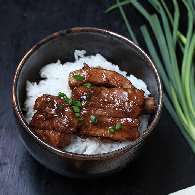un bol chinois avec du riz au fond et des morceaux de porc hong shao par dessus